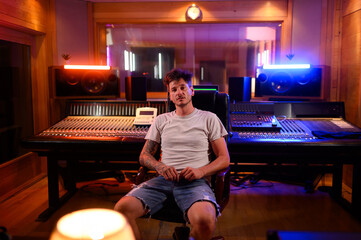 Tattooed man sound engineer sitting in a chair and posing while working a studio