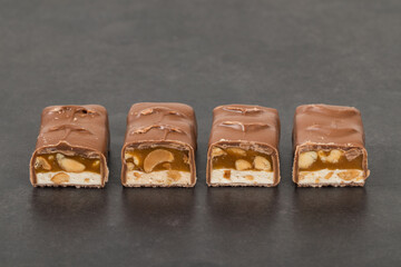 Candy bar. Nougat, caramel with peanuts, in milk chocolate. Dark gray background. Close-up