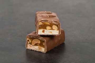 Energy bar. Nougat, caramel with peanuts, in milk chocolate. In the section. Dark gray background. Close-up