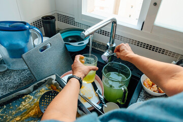 Woman hands wash dirty dishes in sink after cooking or preparing meals. Messy kitchen, household chores, kitchen cleanup after cooking