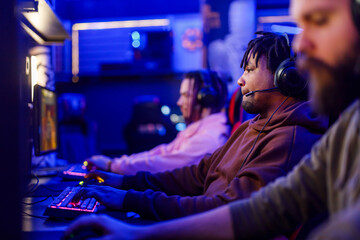 Side view of interracial gamer with headset playing mmo fps in cybercafe