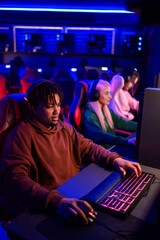 Interracial gamer guy with headset playing strategy games in cybercafe
