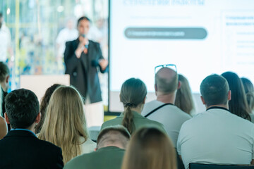 Business professional giving presentation to engaged audience in a modern conference setting. Focus on communication and learning.