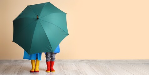 Little children in rubber boots and with umbrella near beige wall. Banner for design