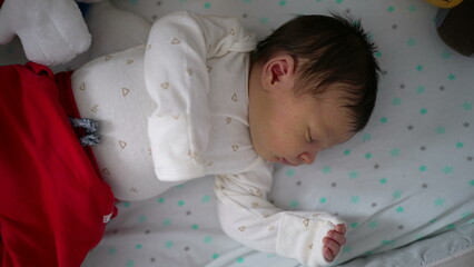 Newborn baby sleeping peacefully on a soft, star-patterned blanket, dressed in a white onesie with tiny triangle prints and red pants, conveying innocence and tranquility