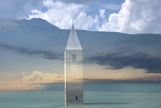 Backpacker on the frosted pier on the lake of Resia (Reschen) in the west of South Tyrol. Curon in Val Venosta, Italy. Sunken steeple towering from the lake.