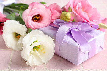 Bouquet of beautiful pink eustoma flowers and gift box on light tile background