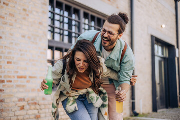 Silly hipster couple with bottles of beverages spilling juice outdoors