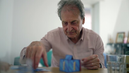 Senior man examining a card from a game, appearing focused and engaged, indoor setting, interaction and concentration during a casual activity