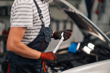 Close up of repairman's hands with gloves holding a wrench at mechanic shop