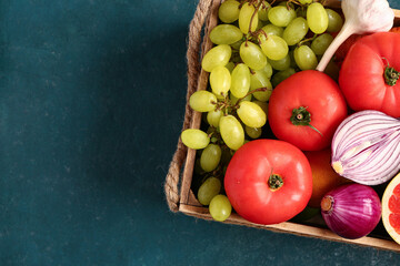 Wooden box with different fresh fruits and vegetables on green background, closeup