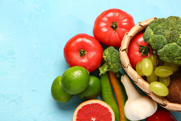 Wicker basket with different fresh fruits and vegetables on blue background, closeup