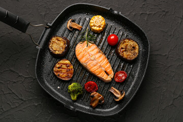 Frying pan with tasty grilled salmon steak and vegetables on black background