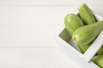 Basket with fresh green zucchini on white wooden background