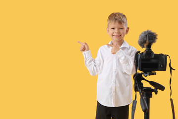 Cute little journalist with camera pointing at something on yellow background