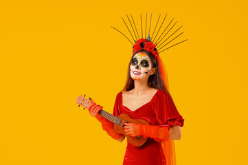 Young woman with painted skull playing guitar on yellow background. Mexico's Day of the Dead (El Dia de Muertos) celebration