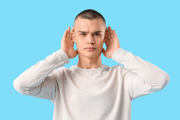 Naklejka premium Teenage boy trying to hear something on blue background