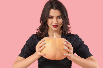 Young witch with pumpkin on pink background