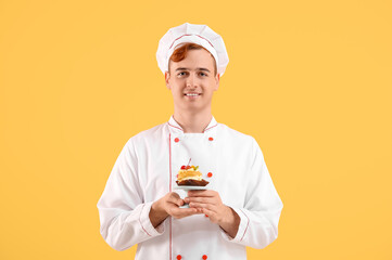 Male confectioner in uniform with tasty profiterole on yellow background