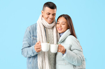 Happy couple in warm clothes with mugs of tasty mulled wine on blue background