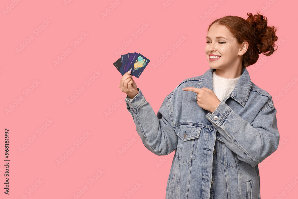 Wall mural beautiful young woman pointing at credit cards on pink background