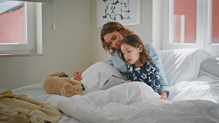 Mother daughter reading book resting together at morning closeup. Happy family