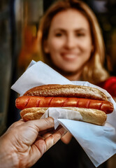 Grilled hot dog on a bun being handed to a customer.