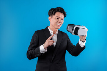 Naklejka premium Smiling Asian businessman looking through VR connecting financial business report futuristic metaverse data analytics power bi technology virtual reality meta isolated blue copyspace. Contrivance.