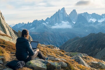 Fototapeta premium An individual sits on a rocky terrain with a stunning view of mountains, working on a laptop surrounded by the awe-inspiring beauty of high-altitude nature.