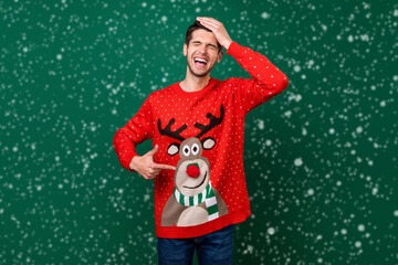 Photo portrait smiling man pointing at funny knitted sweater with reindeer laughing isolated green...