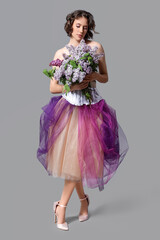 Naklejka premium Beautiful young woman with bouquet of blooming lilac flowers on grey background