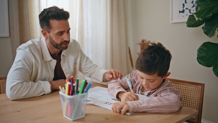 Closeup dad teaching boy doing homework in living room. Small child and parent