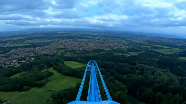 First-person view of a rollercoaster climbing to the top, overlooking a town.