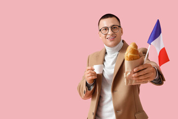 Young man with French flag, croissant and cup of coffee on pink background