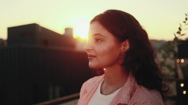 Close up of woman&rsquo;s face indian girl opening her dark eyes with beautiful pink sunset outdoors Pretty inspired young female model with brown eyes looking at sky at home terrace