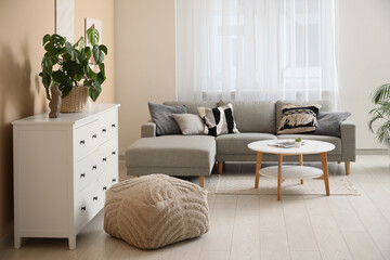 Chest of drawers, cozy sofa and coffee table near beige wall in living room