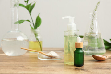 Laboratory glassware with ingredients and samples for preparing natural cosmetics on brown wooden table near white wall