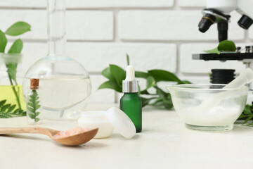 Laboratory glassware and microscope with ingredients for preparing natural cosmetics on white table near brick wall