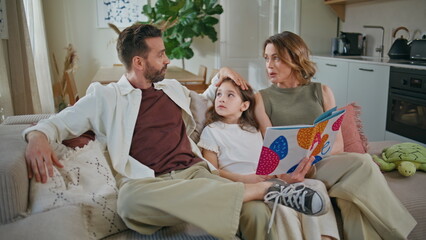 Obraz premium Little girl communicating parents relaxing at sofa. Family reading fairy tale