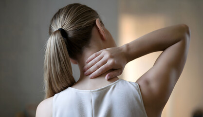 Woman with tied-back hair holding her neck from behind, experiencing neck tension or discomfort, dressed in a sleeveless top