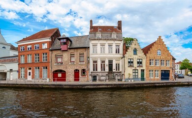 This image features a picturesque canal in Bruges, Belgium. The canal is surrounded by colorful houses and a blue sky with white clouds. The image is perfect for a travel brochure or website.