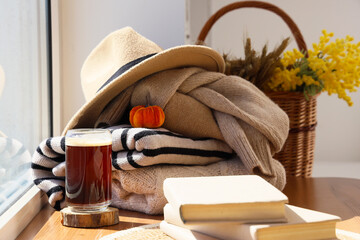 Stack of stylish autumn clothes with books and glass of coffee on table near window at home