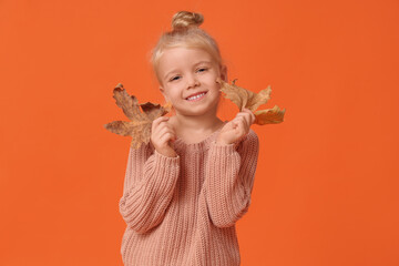 Cute little happy girl in warm stylish sweater with autumn leaves on orange background
