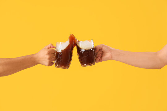 Male hands with glasses of cold beer clinking on yellow background. Octoberfest celebration