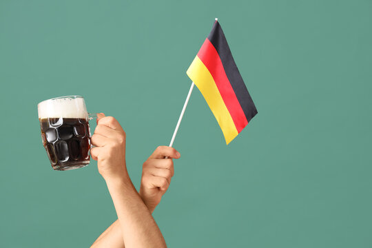 Male hands with mug of cold beer and Germany flag on green background. Octoberfest celebration