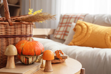 Pumpkin with mushrooms, books and basket on table in cozy living room, closeup