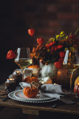 Beautiful elegant table setting for candlelight Thanksgiving Day dinner or Halloween party at home. Fancy dishware, porcelain plates. Floral centrepiece, pumpkins and burning candles as decor