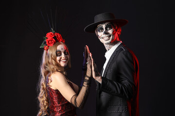 Young happy couple dressed for Mexico's Day of the Dead (El Dia de Muertos) on black background