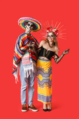 Young happy couple dressed for Mexico's Day of the Dead (El Dia de Muertos) on red background