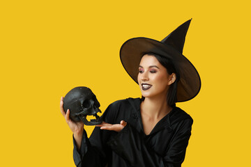 Beautiful young happy witch with black human skull on yellow background